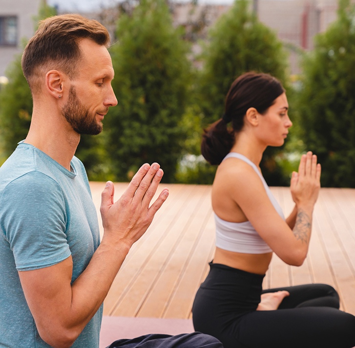 Two caucasian slim adults meditating on yoga class in the garden